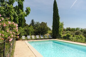 Una piscina rectangular con agua azul cristalina, rodeada por una solana de hormigón. Hay cinco sillas de descanso alineadas a lo largo del borde de la piscina.