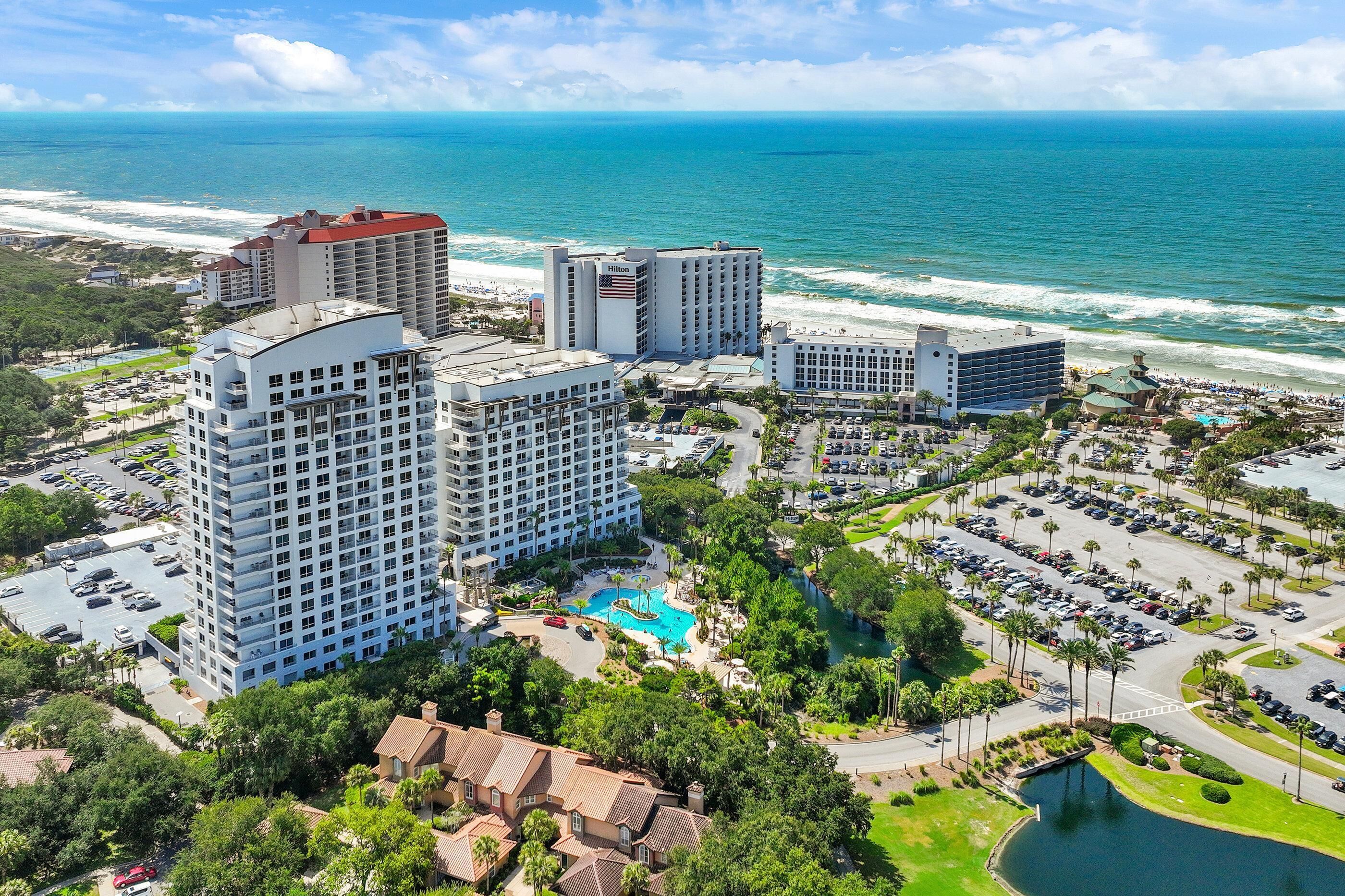A coastal hotel with multiple high-rise buildings, a swimming pool, and a beach view.