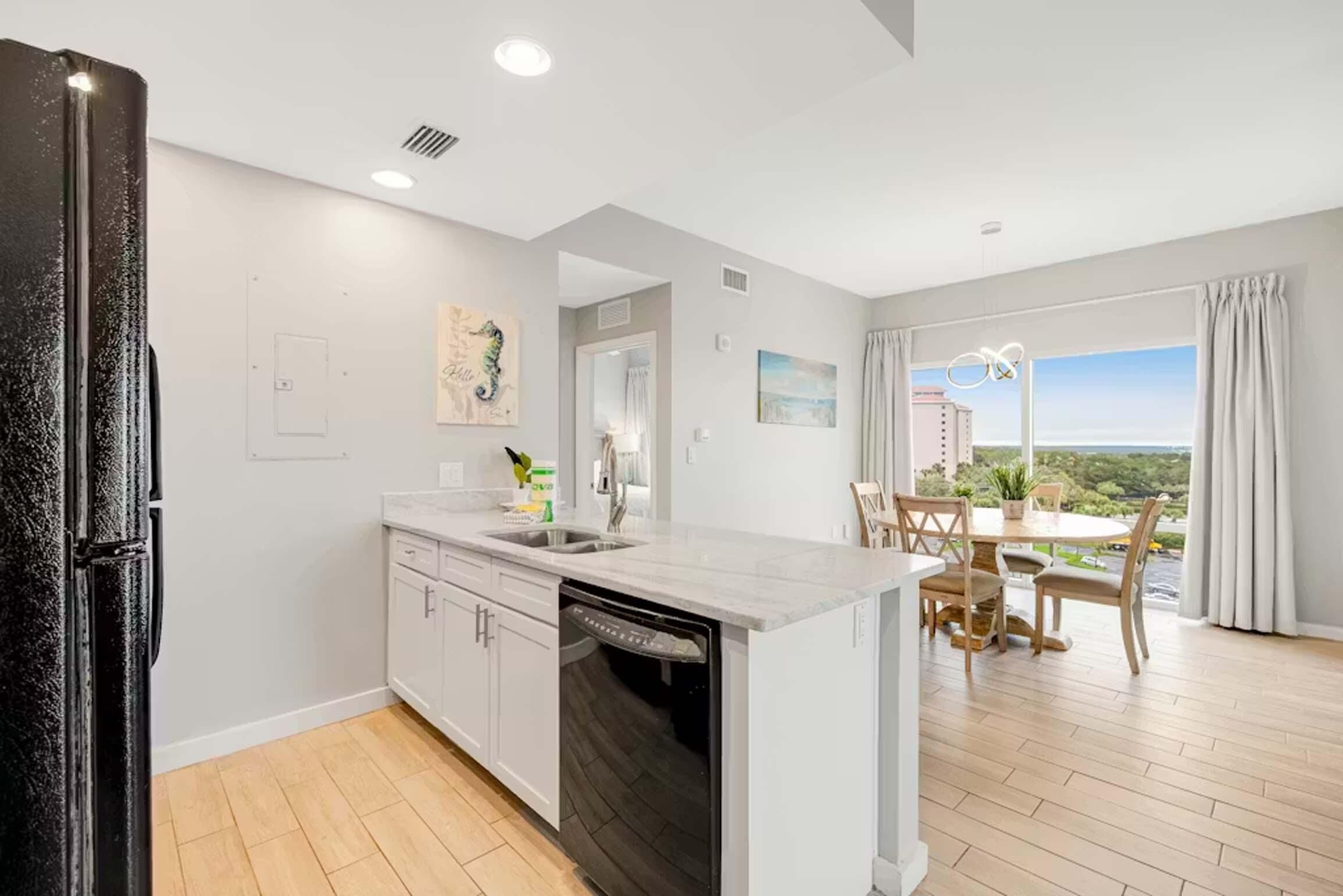 A modern kitchen with a dishwasher, a dining area with a table and chairs, and a view of the outdoors.