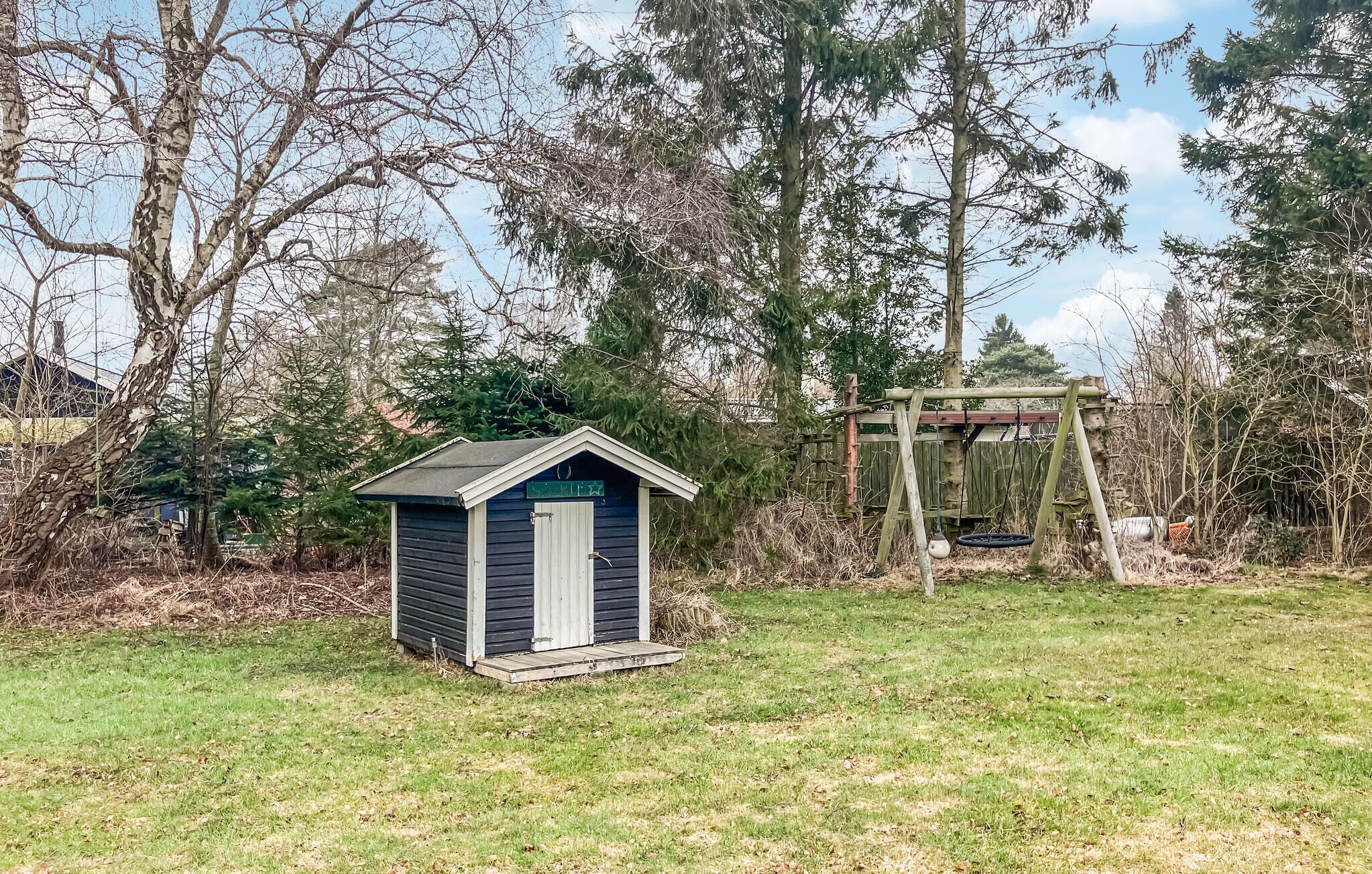 A small shed with a sloped roof and a star-shaped window, surrounded by a grassy yard and trees.