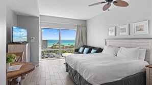 A hotel room with a bed, a desk with a computer, a dining table with chairs, and a view of the ocean. - Luau II 6633 (Miramar Beach)