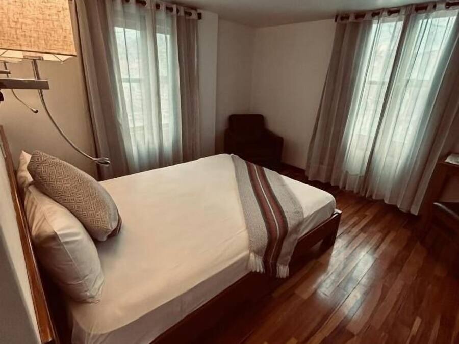 A bedroom with a bed, a chair, a lamp, and curtains.