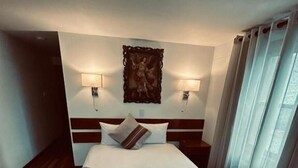 Une chambre d’hôtel avec un lit, un plancher en bois, deux lampes de chevet, une œuvre d’art accrochée au mur et une fenêtre avec des rideaux.