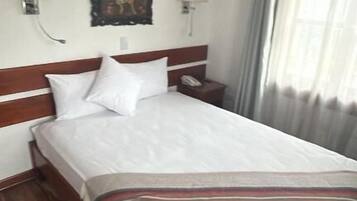 A hotel room with a wooden floor, a large bed with white linens, two wall-mounted lamps, and a painting above the bed.