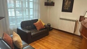 Un salon avec un canapé en cuir foncé, un parquet, un radiateur et un tableau accroché au mur.