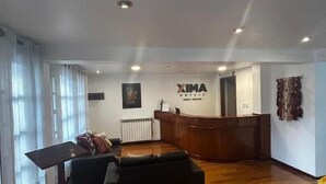 Un vaste espace de vie doté d’un plancher en bois, d’un canapé, d’une petite table et d’un comptoir d’accueil sur lequel est affiché un panneau indiquant « XIMA HOTELS ».