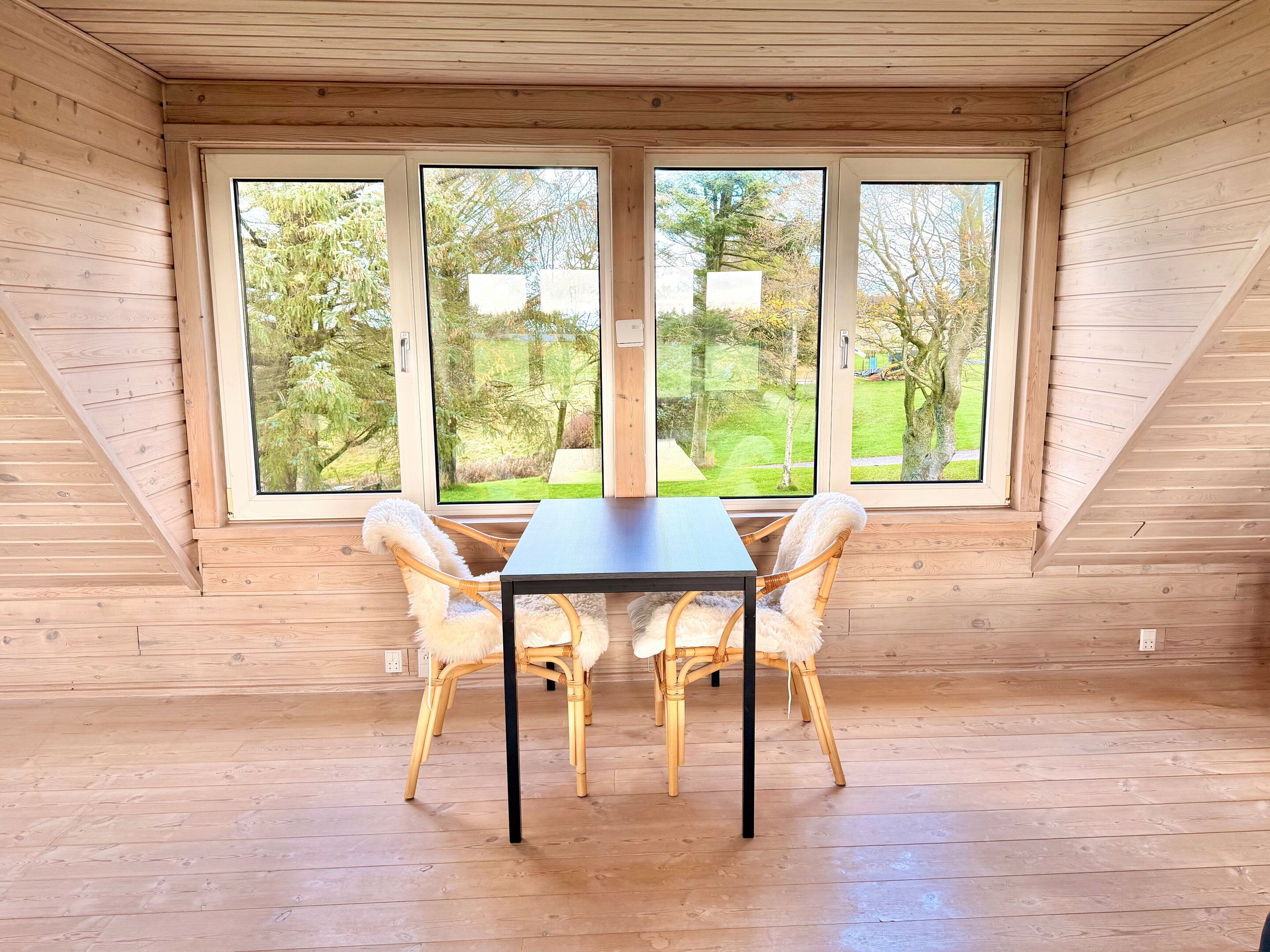 A room with a table and four chairs, large windows, and wooden walls.