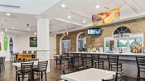 Un restaurante con zona de bar, varias mesas y sillas, y una pantalla de televisión.