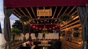 Un área de estar al aire libre con un toldo rojo, luces colgantes y un letrero que dice 'Relax'.
