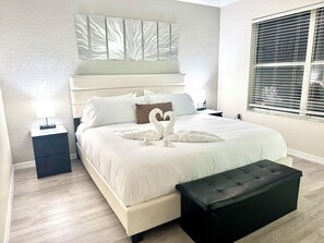 A hotel room with a large bed, a black ottoman, a nightstand with a lamp, and a window with blinds. - 4BR villa at Regal Palms/Lazy River, Pools, Spa/Near Disney (Polk County)