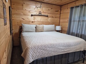 A wooden cabin room with a bed, a headboard, a lamp, and a curtain. - Get away from it all in this beautiful Paradise in Northwest Arkansas! (Kingston)