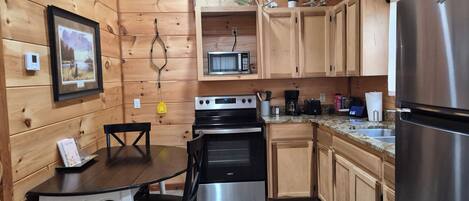 Una cocina tipo cabaña de madera con una mesa de comedor, sillas, estufa, microondas y refrigerador.