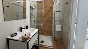 Une salle de bain moderne avec une douche à parois de verre, un lavabo blanc doté d’un cadre noir et un mur recouvert de panneaux en bois.
