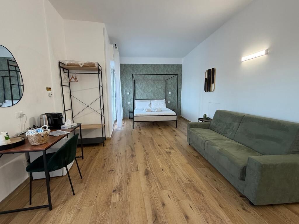 Quarto com cama, sofá verde, escrivaninha com cadeira e pequena mesa com cesta.