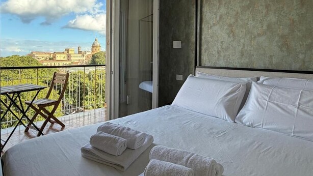 Une chambre d’hôtel avec un lit, un balcon doté d’une table et de chaises, et une vue sur un immeuble.