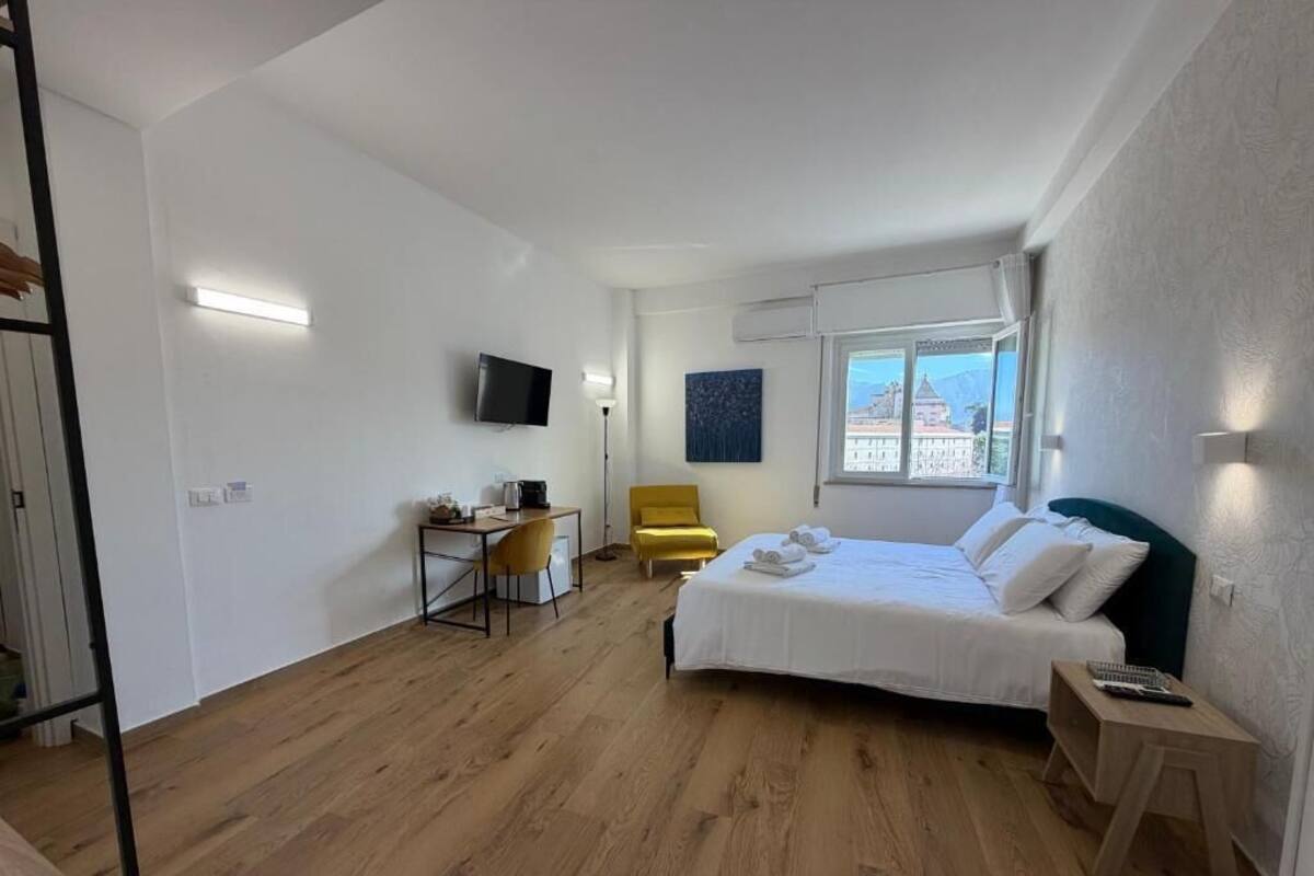 A hotel room with a bed, a desk, a chair, a TV, and a window with a view.