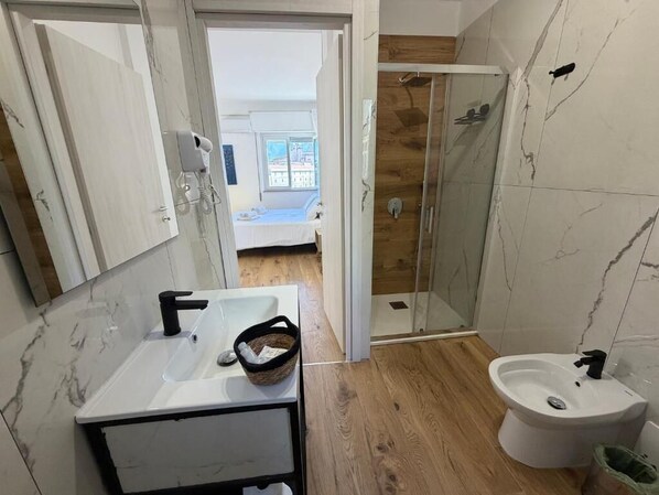 Un baño con lavamanos blanco, un bidé y una cabina de ducha de vidrio.
