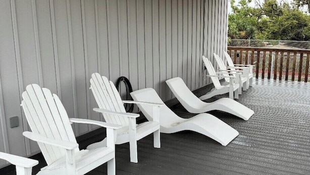 Een overdekt terras met witte Adirondack-stoelen en een houten terras.