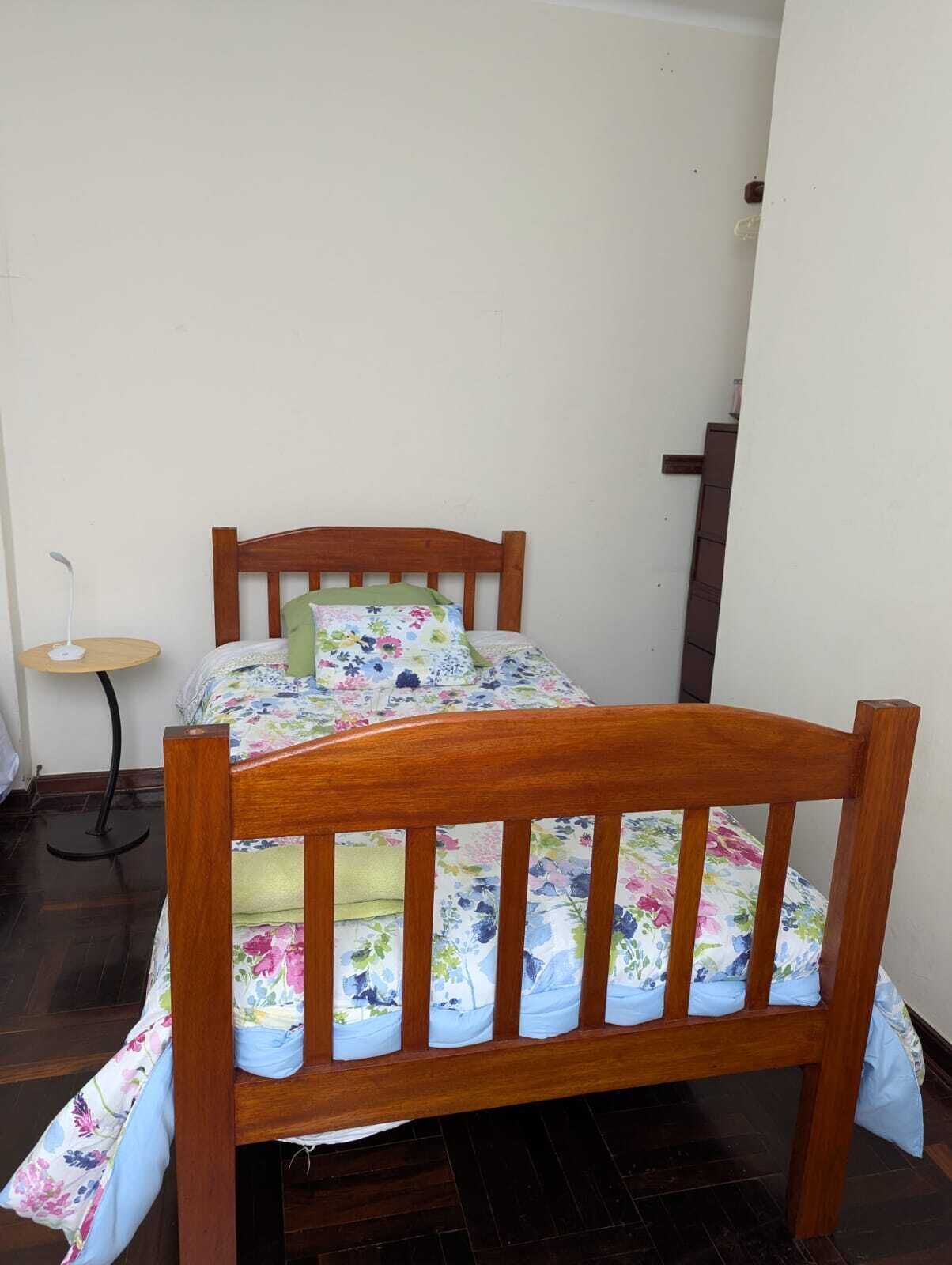 A wooden bed with a floral bedspread in a room with a small round table and a staircase.