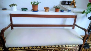 A wooden bench with a white cushion, a white wall, and a shelf with various potted plants and a small black device. - Strategic and centrally located apartment in Magdalena del Mar (Magdalena del Mar)