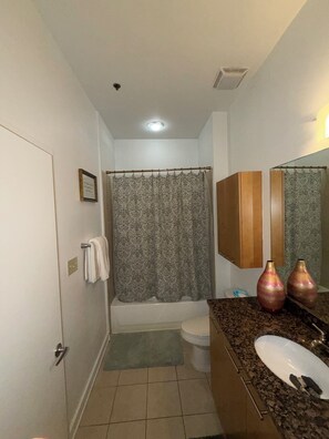 Une salle de bain avec un rideau de douche, des toilettes, un lavabo avec un miroir et un porte-serviettes.