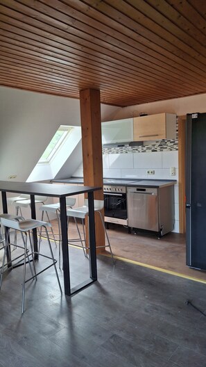 A modern kitchen with a skylight, stainless steel appliances, and a dining area with a table and chairs. - Landhaus Korf - Holiday apartment in the Weserbergland with large balcony (Extertal)
