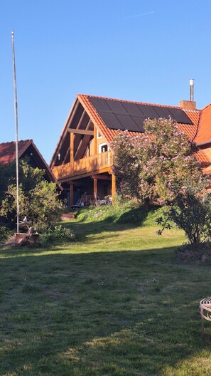 A wooden house with a sloped roof, a balcony, and a chimney. - Landhaus Korf - Holiday apartment in the Weserbergland with large balcony (Extertal)