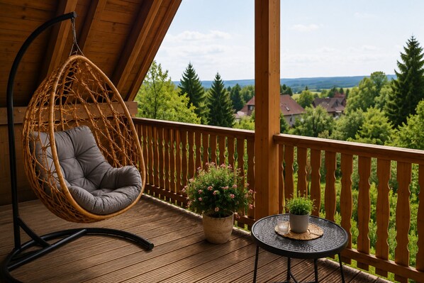 A wooden deck with a hanging chair, a small table with a candle, and potted plants. - Landhaus Korf - Holiday apartment in the Weserbergland with large balcony (Extertal)