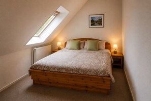 A bedroom with a sloped ceiling, a skylight, a bed with a patterned bedspread, two bedside lamps, and a framed picture on the wall. - Landhaus Korf - Holiday apartment in the Weserbergland with large balcony (Extertal)