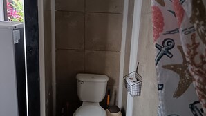 A small bathroom with a toilet, a trash bin, and a window. - Cute studio with AC near Chaman beach Uvita Puntarenas (Uvita)