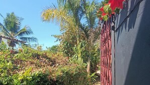 A narrow pathway flanked by dense foliage and a building with a red metal gate. - Cute studio with AC near Chaman beach Uvita Puntarenas (Uvita)