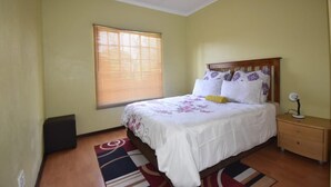 Un dormitorio con cama, mesita de noche, ventana con persianas y lámpara en el techo.