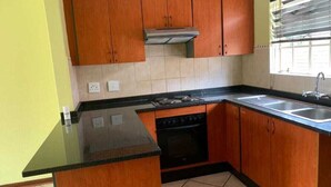 Una cocina con armarios de madera, estufa a gas, pileta y ventana con persianas.