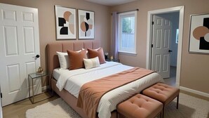 Un dormitorio con cama, banco, mesita de noche y obras de arte en las paredes.
