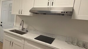 Una cocina con armarios blancos, una campana extractora de acero inoxidable, un lavamanos y una encimera negra.