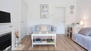 Uma sala de estar moderna com um sofá branco, uma mesa de centro com livros, lareira e televisão.