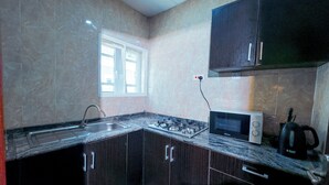Une cuisine avec des meubles de couleur sombre, une cuisinière à gaz, un four à micro-ondes et une fenêtre.