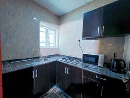 Uma cozinha com armários escuros, fogão a gás, micro-ondas e uma janela.