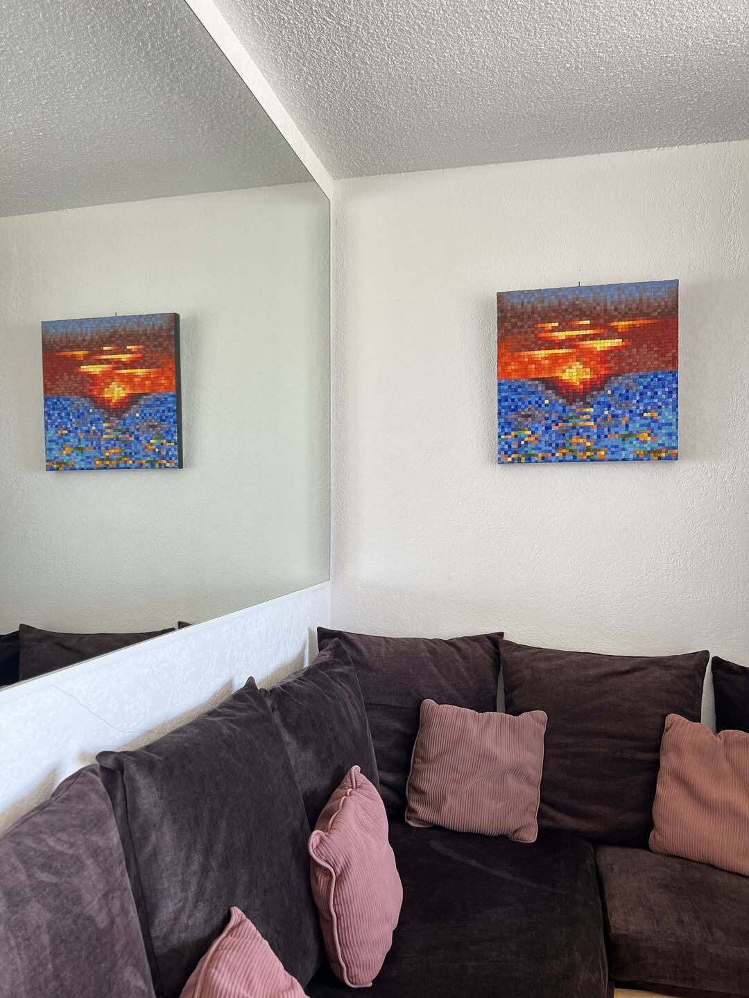 A living room with a dark brown sofa, two cushions, and two paintings on the wall.