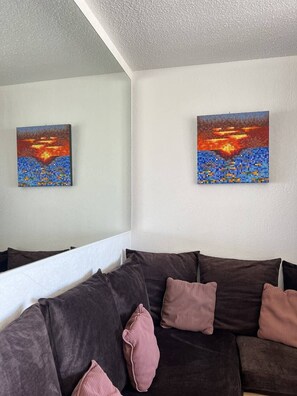A living room with a dark brown sofa, two cushions, and two paintings on the wall. - MALIBU - Héliopolis Apartment O14 - Luxe - 2 people (AGDE)