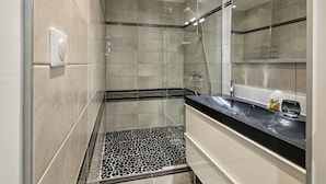 Un bagno moderno con box doccia in vetro, pavimento a scacchi bianco e nero e un piano di lavoro nero con uno specchio.