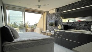 A bedroom with a bed, a desk, and a kitchenette. - CAP-Y-SUN - Studio Héliopolis O18 - Luxe - 2 people (AGDE)