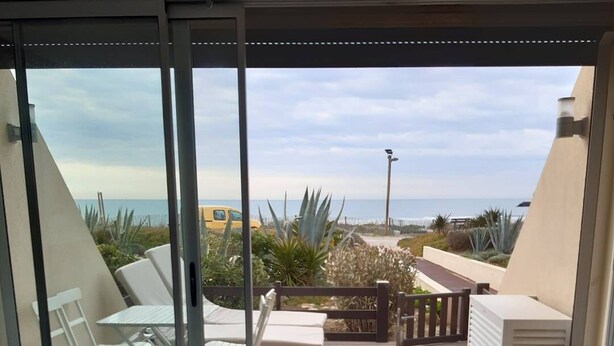 A balcony with a view of the beach, a table, chairs, and a bed. - CAP-Y-SUN - Studio Héliopolis O18 - Luxe - 2 people (AGDE)
