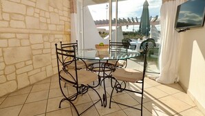 A dining area with a glass table and metal chairs, a wicker basket, and a view of a building through a glass door. - SESAME - Apartment Port Ambonne PA122 - Luxe - 4 people (AGDE)