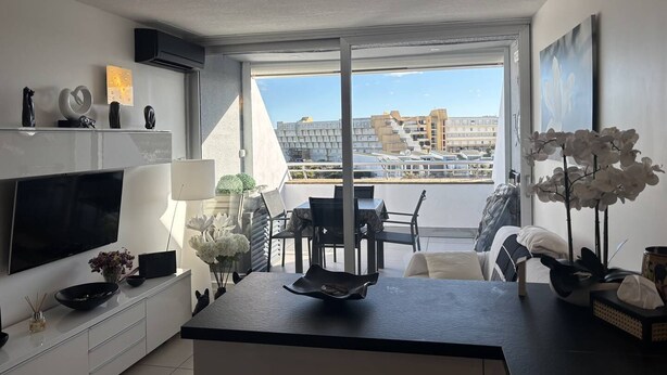 A modern kitchen with a flat-screen TV, a dining area with a table and chairs, and a balcony with a view of buildings. - ZEN - Port Ambonne Apartment  PA311 - Luxury - 2 people (AGDE)