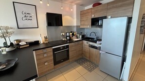 A modern kitchen with wooden cabinets, a black countertop, a stainless steel refrigerator, and a black microwave. - ZEN - Port Ambonne Apartment  PA311 - Luxury - 2 people (AGDE)