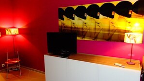 Une pièce avec un téléviseur posé sur un meuble blanc, un mur rouge et un grand tableau abstrait.