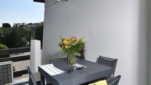 Une terrasse sur le toit avec une table et des chaises, un vase rempli de fleurs et une serviette jaune posée sur une chaise.