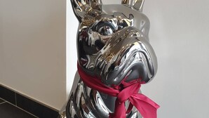 Une sculpture métallique représentant un chien, ornée d’un ruban rouge.