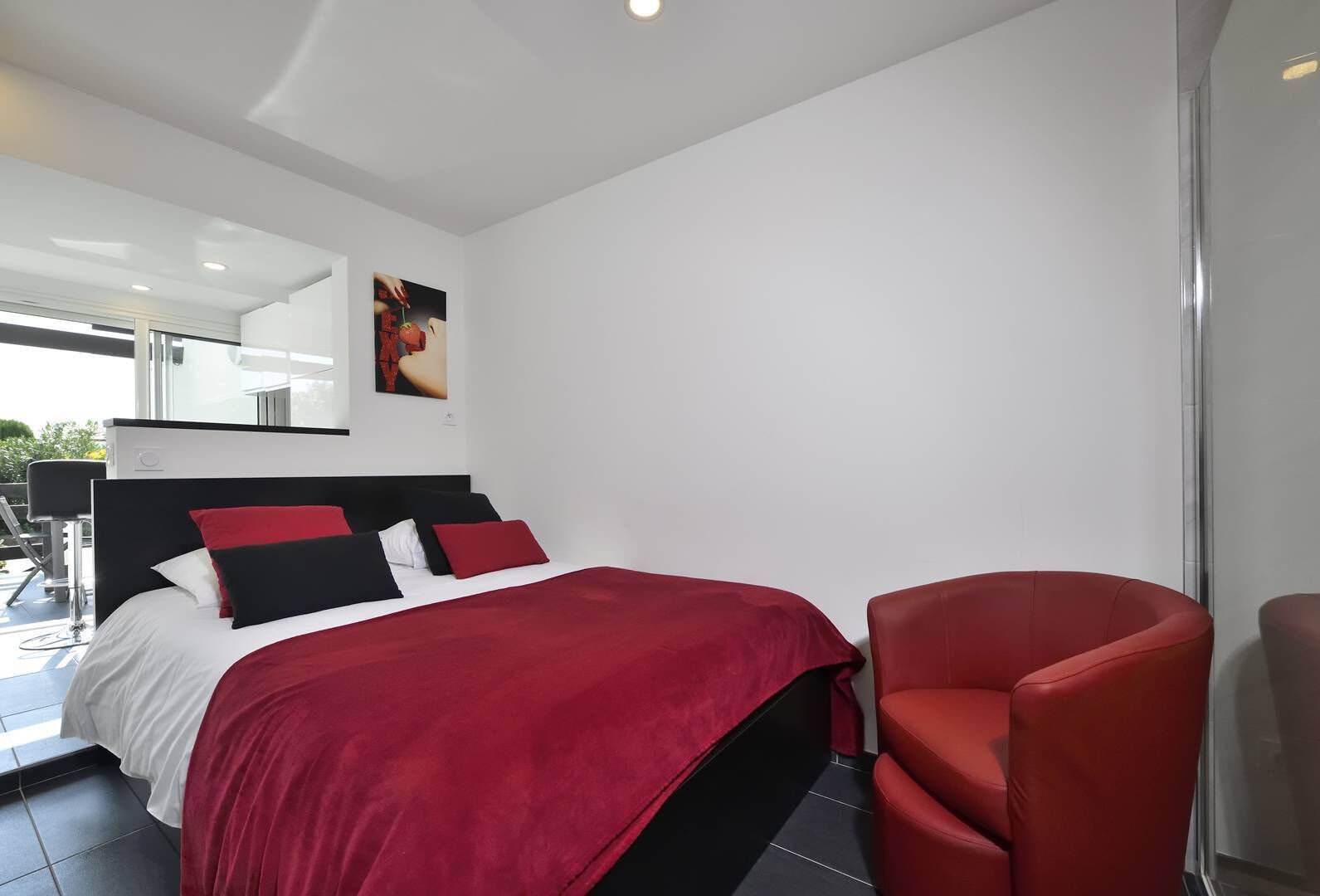 A modern bedroom with a bed, a red chair, and a large window.